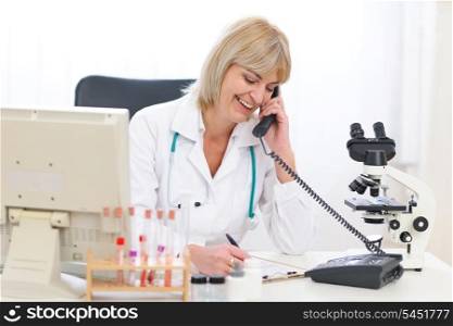Smiling senior doctor woman speaking phone at office