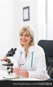 Smiling senior doctor woman working with microscope at laboratory
