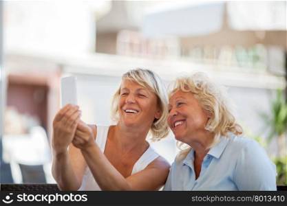Smiling senior female friends taking selfie outdoor using smart phone. Cheerful women making happy shots, copy space above