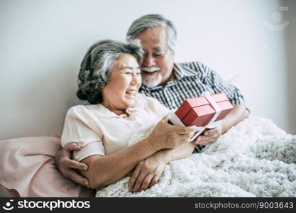 Smiling senior husband making surprise giving gift box to his wife in bedroom