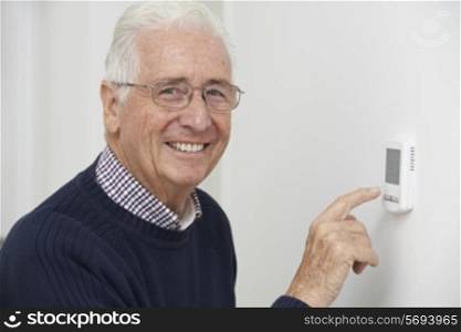 Smiling Senior Man Adjusting Central Heating Thermostat