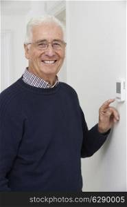 Smiling Senior Man Adjusting Central Heating Thermostat