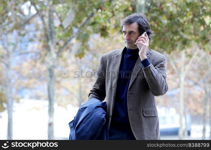 Smiling senior man, businessman talking on the phone while walking around the city, enjoying a corporate mobile conversation
