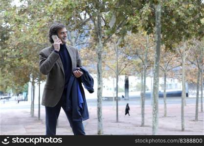 Smiling senior man, businessman talking on the phone while walking around the city, enjoying a corporate mobile conversation