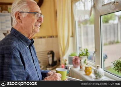 Smiling Senior Man Looking Out Of The Window Holding Cup
