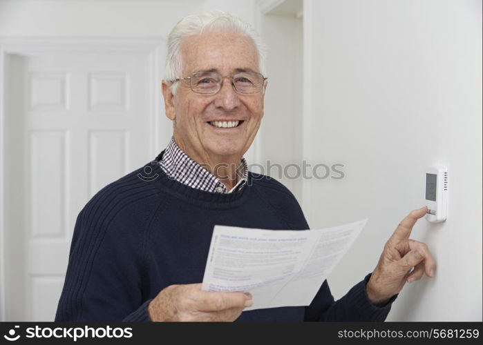 Smiling Senior Man With Bill Adjusting Central Heating Thermostat