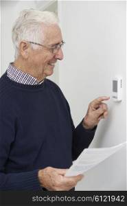 Smiling Senior Man With Bill Adjusting Central Heating Thermostat