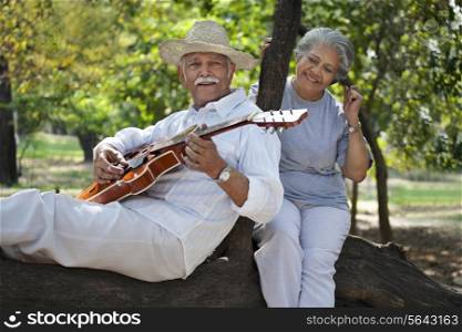 Smiling senior man with woman having fun at park while playing guitar