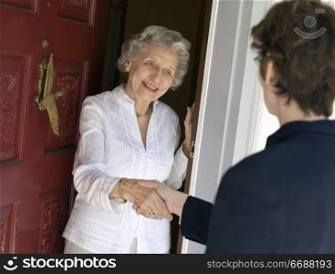 Smiling senior woman greeting visitor at the front door