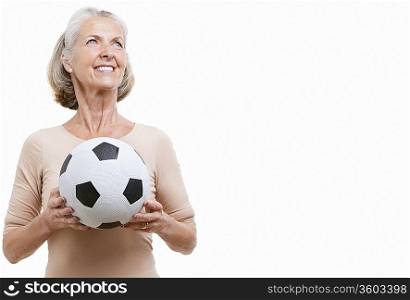 Smiling senior woman in casuals holding soccer ball against white background