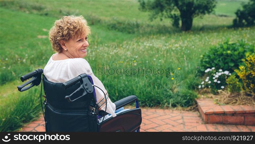 Smiling senior woman in wheelchair in the garden. Senior woman in wheelchair