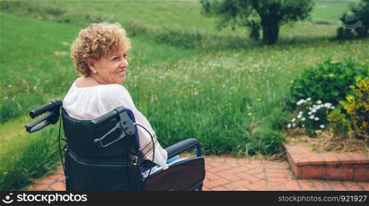 Smiling senior woman in wheelchair in the garden. Senior woman in wheelchair