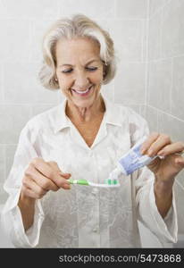 Smiling senior woman squeezing toothpaste on toothbrush in bathroom
