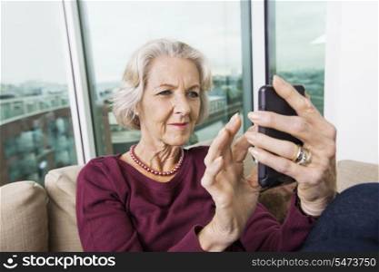 Smiling senior woman text messaging on smart phone at home