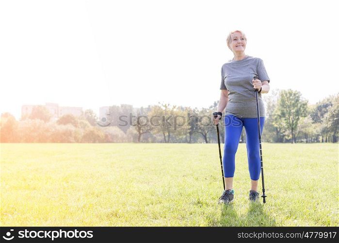 Smiling senior woman using trekking poles while walking in park