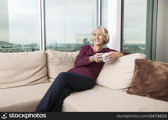 Smiling senior woman with coffee mug relaxing on sofa at home
