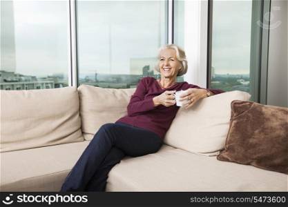 Smiling senior woman with coffee mug relaxing on sofa at home