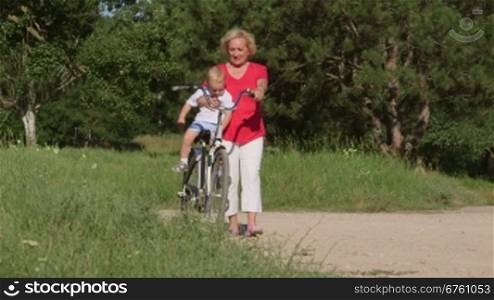 Smiling senior woman with grandson enjoying time together on bicycle in the summer park