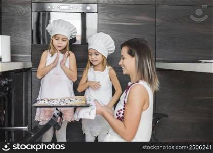 smiling siblings looking mother holding fresh baked cookies tray