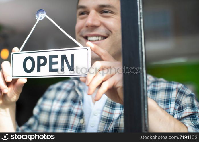 Smiling Small Business Owner Turning Around Open Sign On Shop Or Store Window Or Door