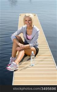Smiling sport woman relax on pier lake sunny day