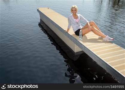 Smiling sport woman relax on pier water sunny day