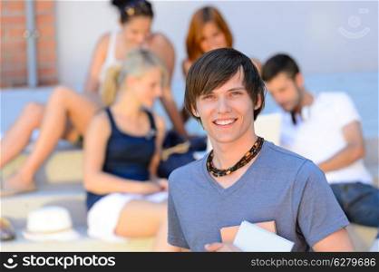 Smiling student boy with friends outside college holding books summer
