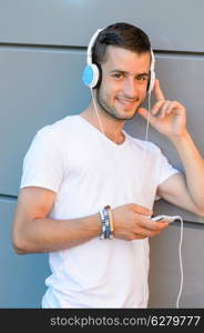 Smiling student boy with headphones standing by modern college wall