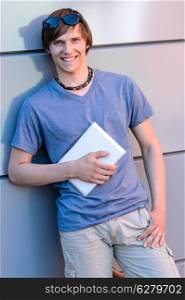 Smiling student boy with tablet leaning against modern wall
