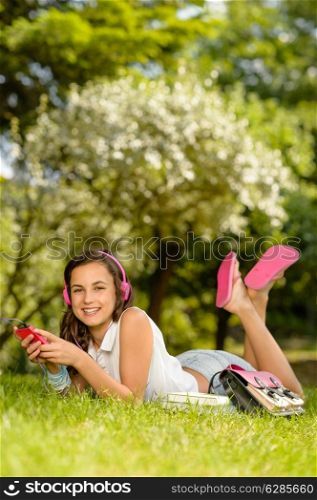 Smiling student girl lying in summer park listen to music