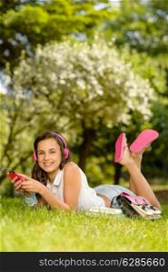 Smiling student girl lying in summer park listen to music