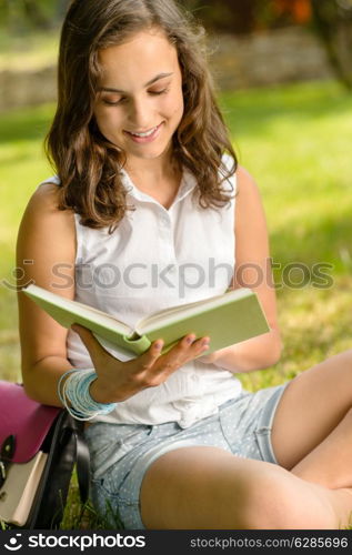 Smiling student girl reading book in park summer