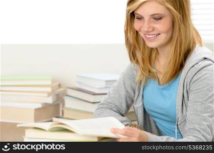 Smiling student girl reading book looking down sitting behind desk