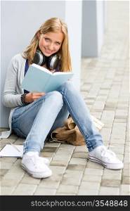 Smiling student girl reading book outside of school sitting ground