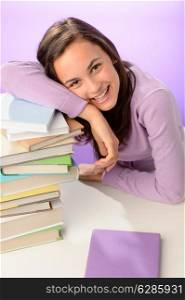 Smiling student girl resting head on stack of books purple background