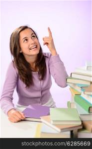 Smiling student girl stack of books pointing up purple background