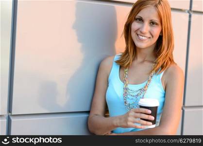 Smiling student girl with coffee cup summer standing by wall