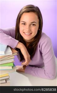 Smiling student girl with pile of books on purple background