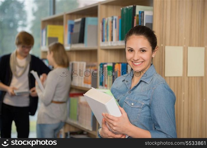 Smiling student holding books in front of bookshelf at library