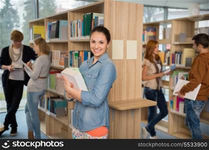 Smiling student holding books with friends talking in college library