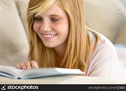 Smiling student teenager reading book lying on sofa