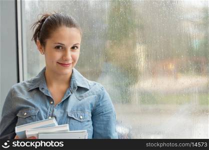 Smiling student with books in front of wet window