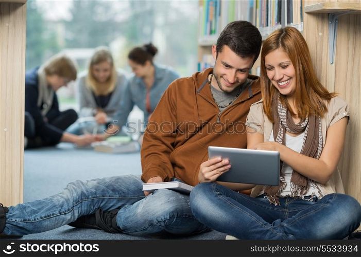 Smiling students using tablet with friends in background at library