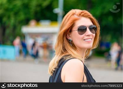 Smiling stylish girl in sunglasses in a city park