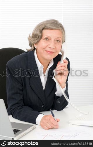 Smiling successful senior businesswoman sitting behind office table portrait