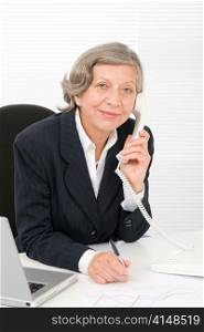 Smiling successful senior businesswoman sitting behind office table portrait