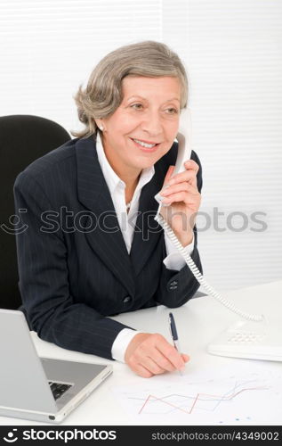 Smiling successful senior businesswoman sitting behind office table portrait