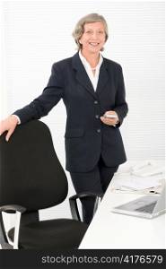 Smiling successful senior businesswoman standing behind office table portrait