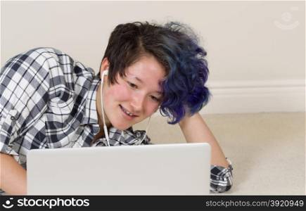 Smiling teen girl looking at computer while listening to music at home.