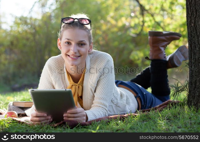 smiling teen girl lying with tablet pc under the tree in evening sunlight outdoors